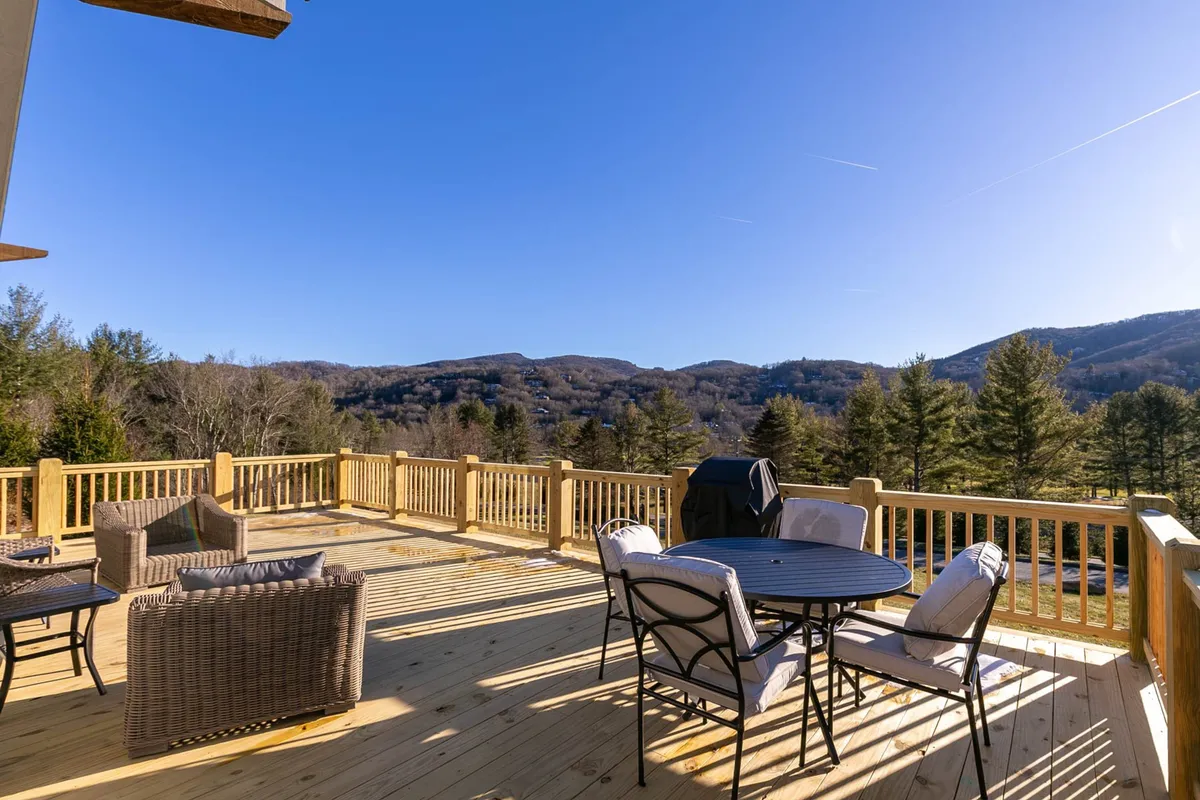 A tranquil deck scene with stylish furniture arranged for outdoor dining and relaxation, a gas grill ready for a barbecue, and sweeping mountain vistas. The setting suggests opportunities for both social gatherings and quiet moments in nature.
