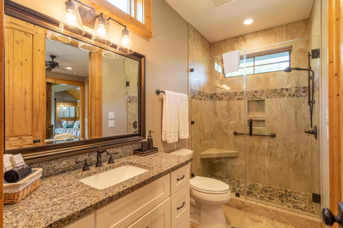 A stylish bathroom with a granite countertop, framed mirror, glass shower enclosure, and wooden accents. The space evokes a spa-like feel, perfect for rejuvenating after a day outdoors.