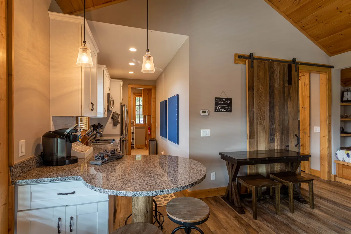 A stylish, open kitchen showcasing granite countertops, a wooden barn door, pendant lighting, and modern appliances. The layout invites conversation at the breakfast bar, with subtle details like a coffee maker on the counter, tying in elements of morning rituals and casual dining.