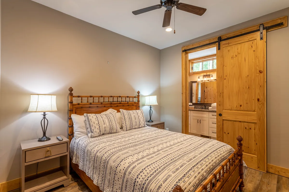 A tranquil bedroom scene featuring a comfortable bed with patterned bedding, wooden sliding door, and nightstands with softly glowing lamps. Natural light streams into the room, creating a serene, relaxing space ideal for restful sleep.