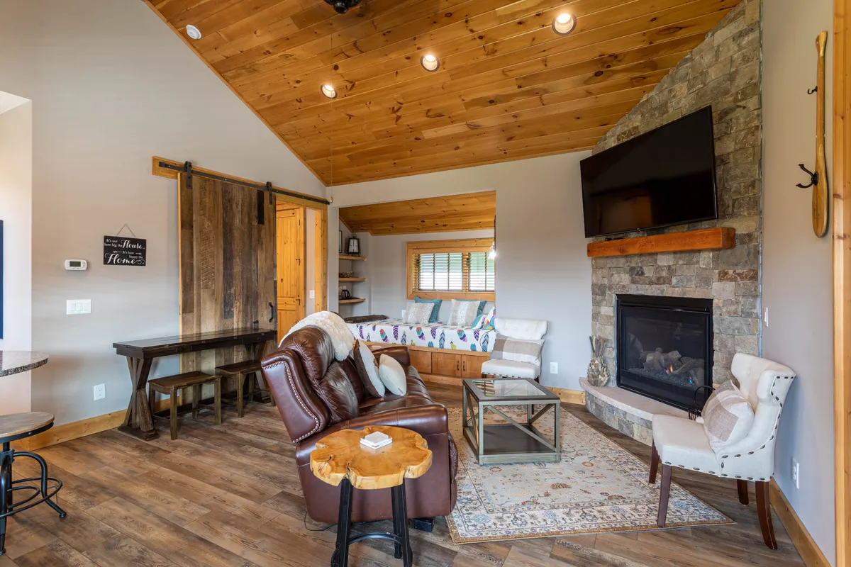 A warmly lit living area featuring a stone fireplace, comfortable sofa, and wooden accents, with plenty of natural light filtering in. The scene invites relaxation and togetherness, ideal for unwinding after a day exploring the mountains.