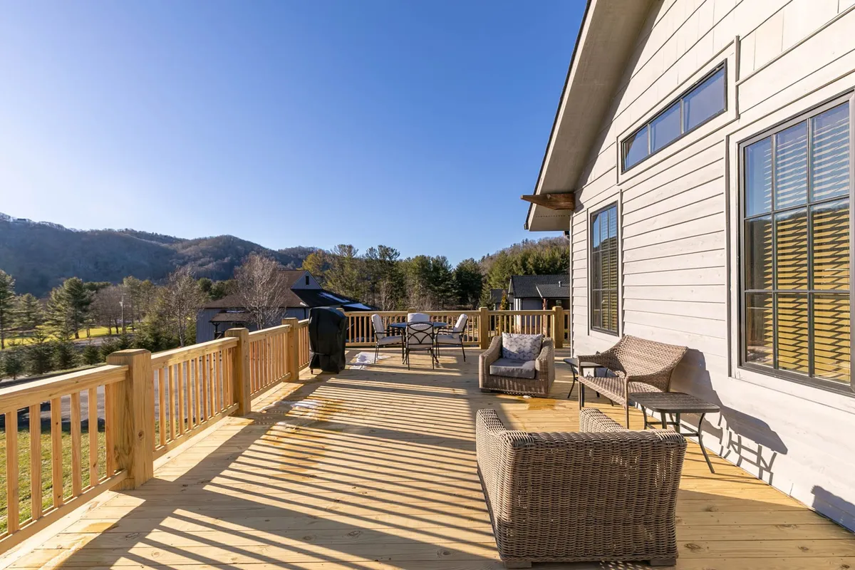 A spacious wooden deck featuring comfortable outdoor seating, a gas grill, and an expansive view of the Blue Ridge Mountains. The scene is set for relaxation or entertaining, with the serene mountain landscape in the background.