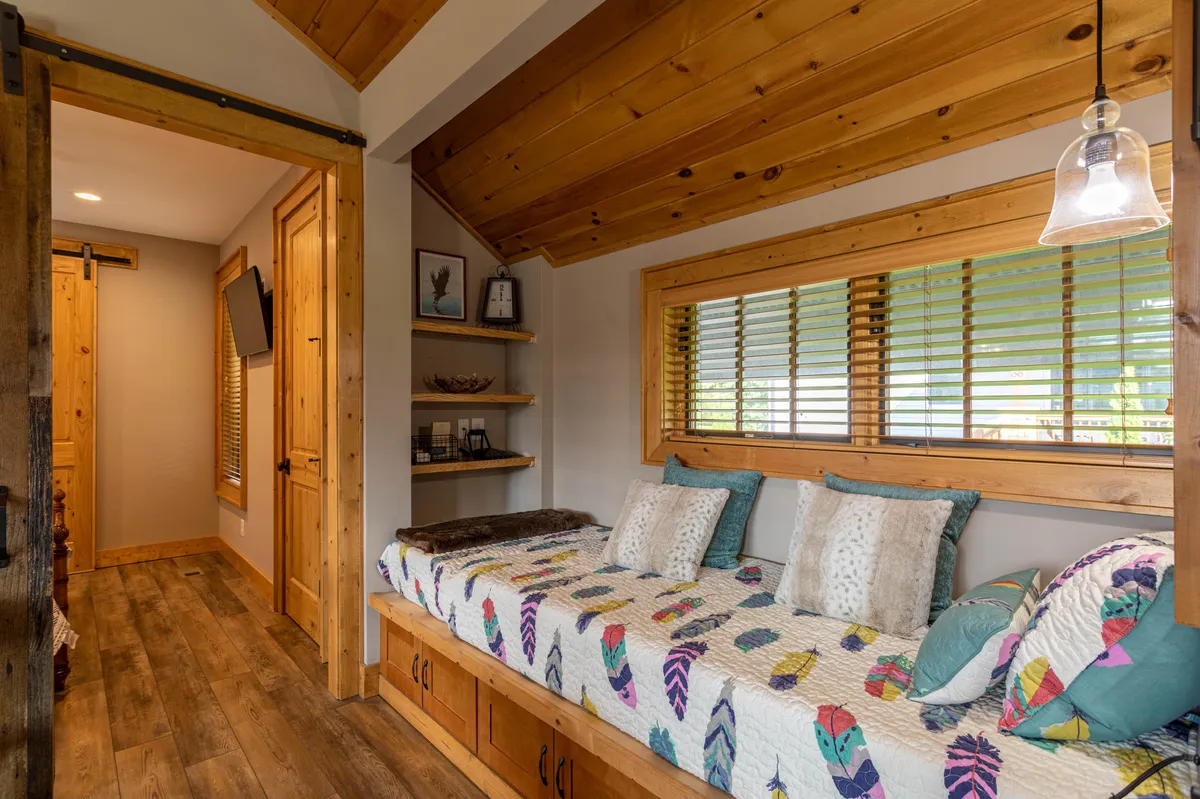 A cozy nook featuring a colorful quilt on a daybed (twin-sized), wooden blinds on the window, and shelves with decorative items. The nook is perfect for reading, relaxing, or as a charming hideaway for children.