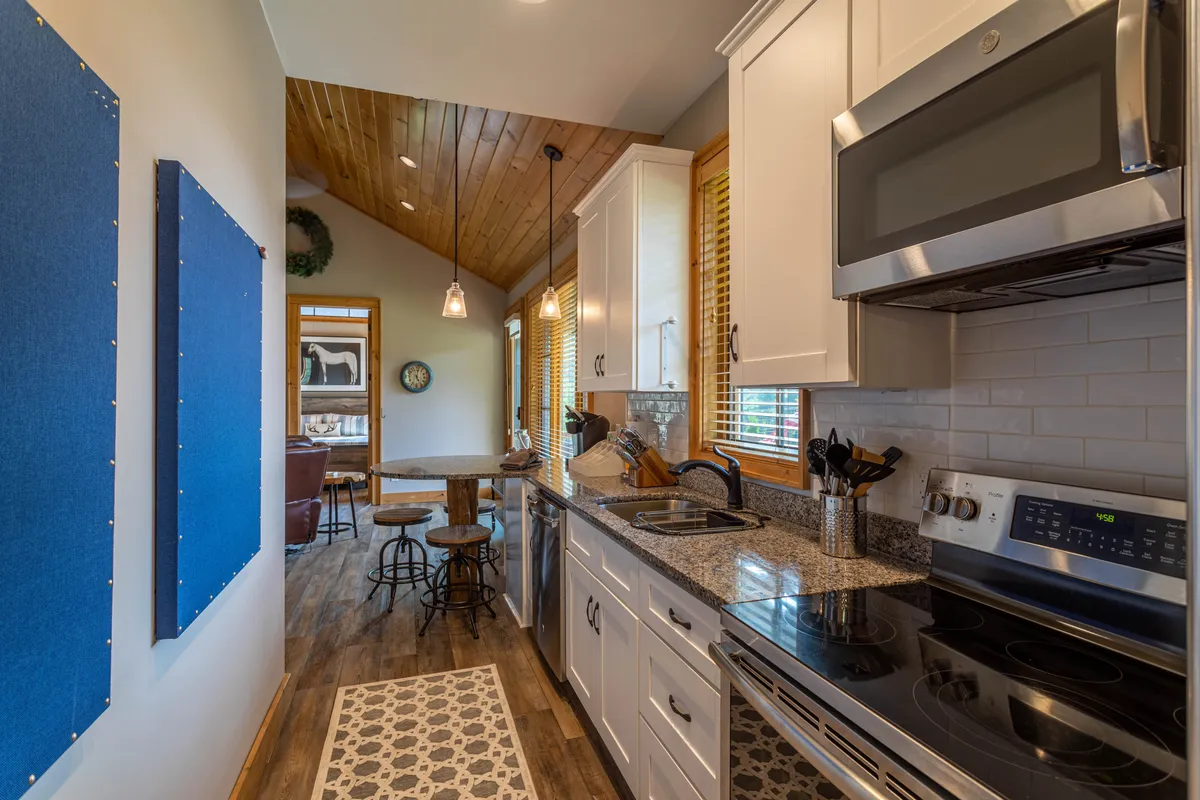 A welcoming kitchen and dining space featuring a sleek granite countertop, modern stainless steel appliances, blue fabric wall art, and a warm wooden dining table set for a meal. The scene suggests a place for both cooking and gathering, with a cozy, inviting atmosphere perfect for family dinners or intimate meals.